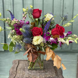 Mixed bouquet with red roses, purple orchids, and blue thistle in a glass vase