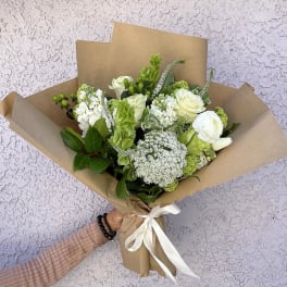 Bouquet of white and green flowers wrapped in brown paper with a white ribbon