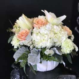 Peach roses and white lilies arranged in a white vase