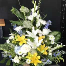Large mixed floral arrangement with white lilies, yellow lilies, and blue flowers