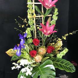 Tall tropical flower arrangement with pink lilies, red roses, and purple irises