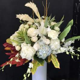 White floral arrangement in a tall vase with tropical leaves and branches