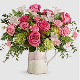Pink roses and white flowers arranged in a glass pitcher vase