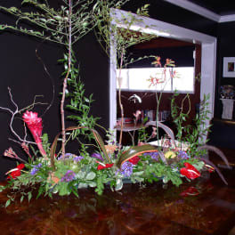 Large tropical floral centerpiece with red blooms and tall branches on a table