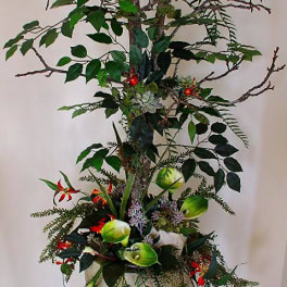 Tall floral arrangement with branches, red blooms, and green calla lilies in a white vase