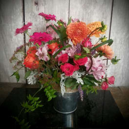 Mixed bouquet of pink, orange, and peach flowers in a metal bucket