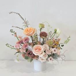 Asymmetrical arrangement of peach and blush flowers in a white cylinder vase