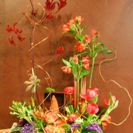 Tall floral arrangement with pink tulips, orange roses, and red tropical blooms