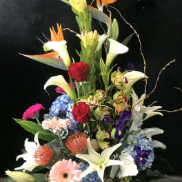 Tall tropical flower arrangement with lilies, roses, and orchids