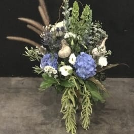 Tall floral arrangement with blue hydrangeas, white blooms, and dried grasses