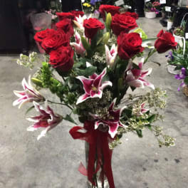 Red roses and pink lilies in a clear glass vase with a red ribbon