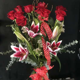 Bouquet of red roses and pink lilies with a polka-dot ribbon in a glass vase