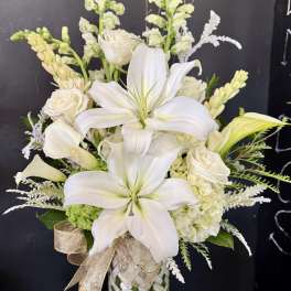 White lilies, roses, and calla lilies in a woven vase with a gold ribbon.