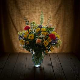 Mixed bouquet of yellow, red, pink, and purple flowers in a glass vase