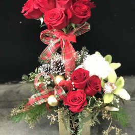 Red roses arranged in a festive holiday centerpiece with ribbon and ornaments