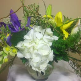 Bouquet of white hydrangea, purple iris, and yellow lilies in a glass vase