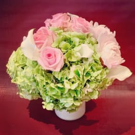 Pink roses and white calla lilies in a white vase with green hydrangeas