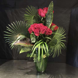 Tall bouquet of red roses in a glass vase with tropical leaves
