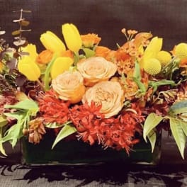 Orange and yellow floral arrangement in a low rectangular container