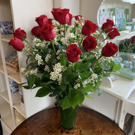 Red roses arranged in a tall green vase with small white filler flowers.