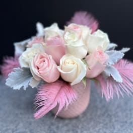Pink and white roses arranged in a small round vase with feathers