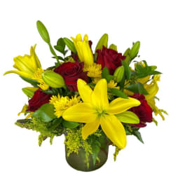 Yellow lilies and red roses arranged in a glass vase