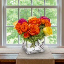 Bouquet of orange, yellow, and pink roses in a square glass vase