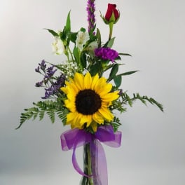 Sunflower bouquet in a clear glass vase with purple ribbon