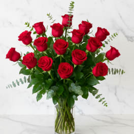 Red roses arranged in a clear glass vase with greenery