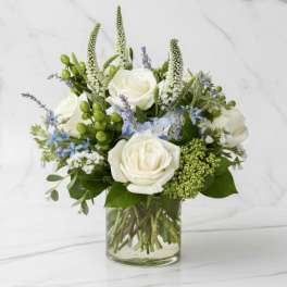 White roses and blue flowers arranged in a clear glass vase