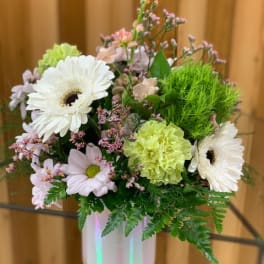 Pastel flower arrangement in a white vase with white daisies and green carnations