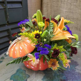 Autumn floral arrangement in a pumpkin-shaped container with lilies and chrysanthemums