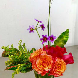 Orange roses and purple flowers in a green glass vase