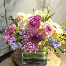 Mixed bouquet of pink, purple, yellow, and white flowers in a glass vase