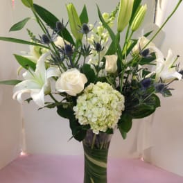 White lilies and roses in a tall glass vase with blue thistle accents