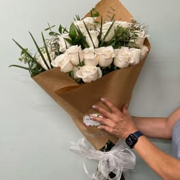 Bouquet of white roses wrapped in brown paper with a white ribbon