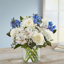 White roses and blue flowers arranged in a clear glass vase