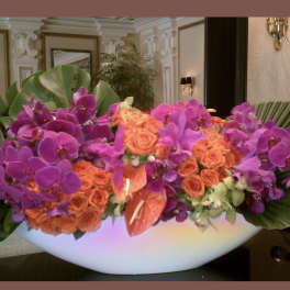 Large arrangement of purple orchids and orange roses in a white bowl vase