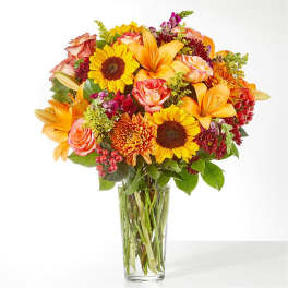 Mixed bouquet of sunflowers, lilies, roses, and chrysanthemums in a clear glass vase