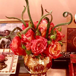 Pink and coral roses in a gold glass vase with curly green stems