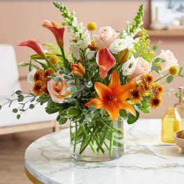 Mixed bouquet of orange lilies, roses, and white blooms in a glass vase