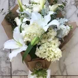 White lily and hydrangea bouquet wrapped in brown paper with a white ribbon