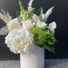 White floral arrangement in a pale cylindrical vase with green accents