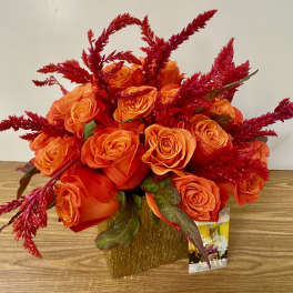 Orange roses in a gold vase with red feathery accents