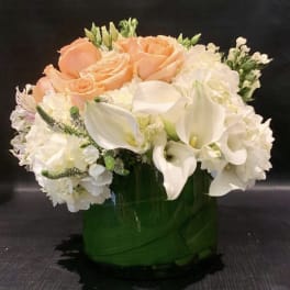 Peach roses and white calla lilies in a green glass vase