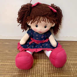 Plush doll with brown yarn hair, blue dress, and pink shoes