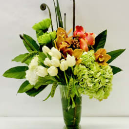 Mixed floral arrangement in a glass vase with green hydrangea and orchids