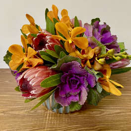 Bright mixed bouquet with orange orchids and purple ornamental cabbage in a low vase
