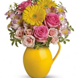 Pink roses and yellow daisies in a yellow pitcher vase
