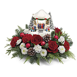 Christmas floral arrangement with red roses, white flowers, and a miniature winter village